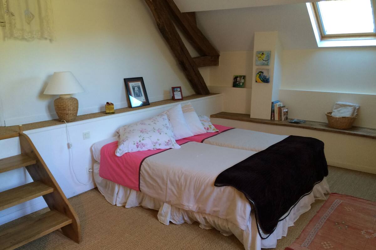 A bedroom with a bed, a lamp, a wooden staircase, and a window.