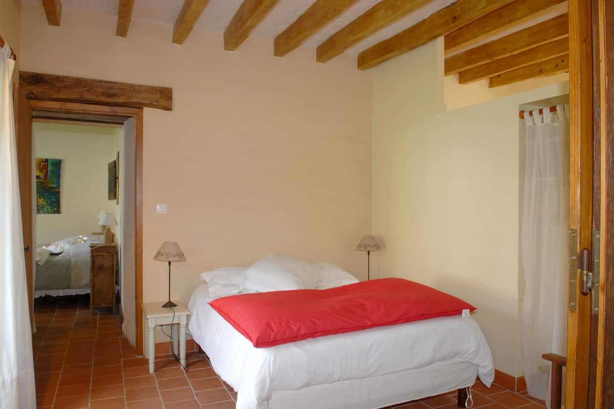 A bedroom with a bed, two bedside lamps, a wooden ceiling, and a tiled floor.