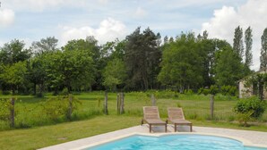 Une piscine avec deux chaises longues en bois et un chemin de pierre menant à la piscine.