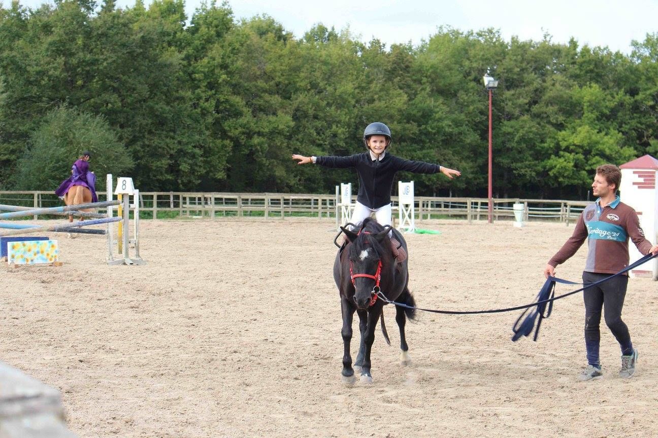 A person riding a horse in an outdoor arena with a sandy ground, surrounded by a fence and trees in the background.