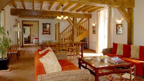 Un vaste salon doté d’un haut plafond en bois, un coin repas avec des meubles en bois, et un escalier menant à un autre niveau.