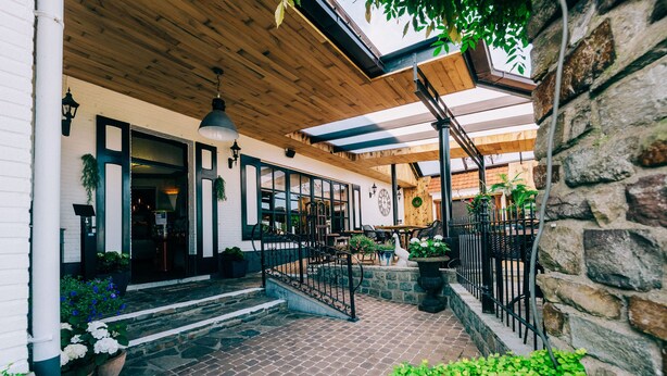 A covered outdoor area with a wooden ceiling, stone walls, and potted plants. - De Kalvaar Hotel (Ninove)