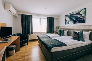 A hotel room with a bed, a desk with a computer, a chair, a TV, and a window with curtains. - De Kalvaar Hotel (Ninove)