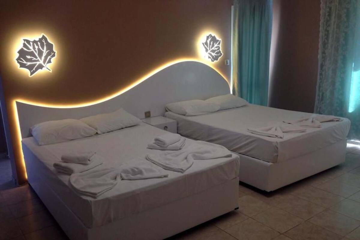A hotel room with two beds, each with white linens and pillows. There are decorative leaf-shaped lights on the wall above the beds.