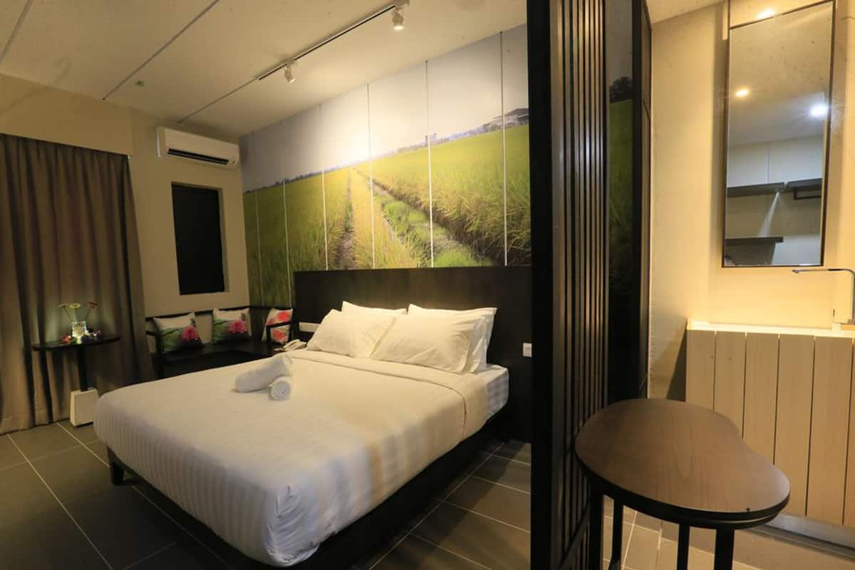 A modern hotel room with a large bed, a small table, a mirror, and a wall-mounted air conditioner.