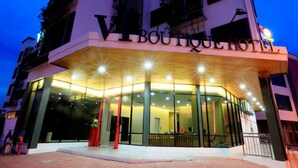 Entrada moderna de hotel com fachada de vidro, um letreiro destacado acima da entrada e interior bem iluminado visível pelas janelas.