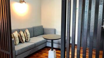 Une pièce avec un canapé gris, des coussins à motifs, une table ronde et un luminaire fixé au mur.