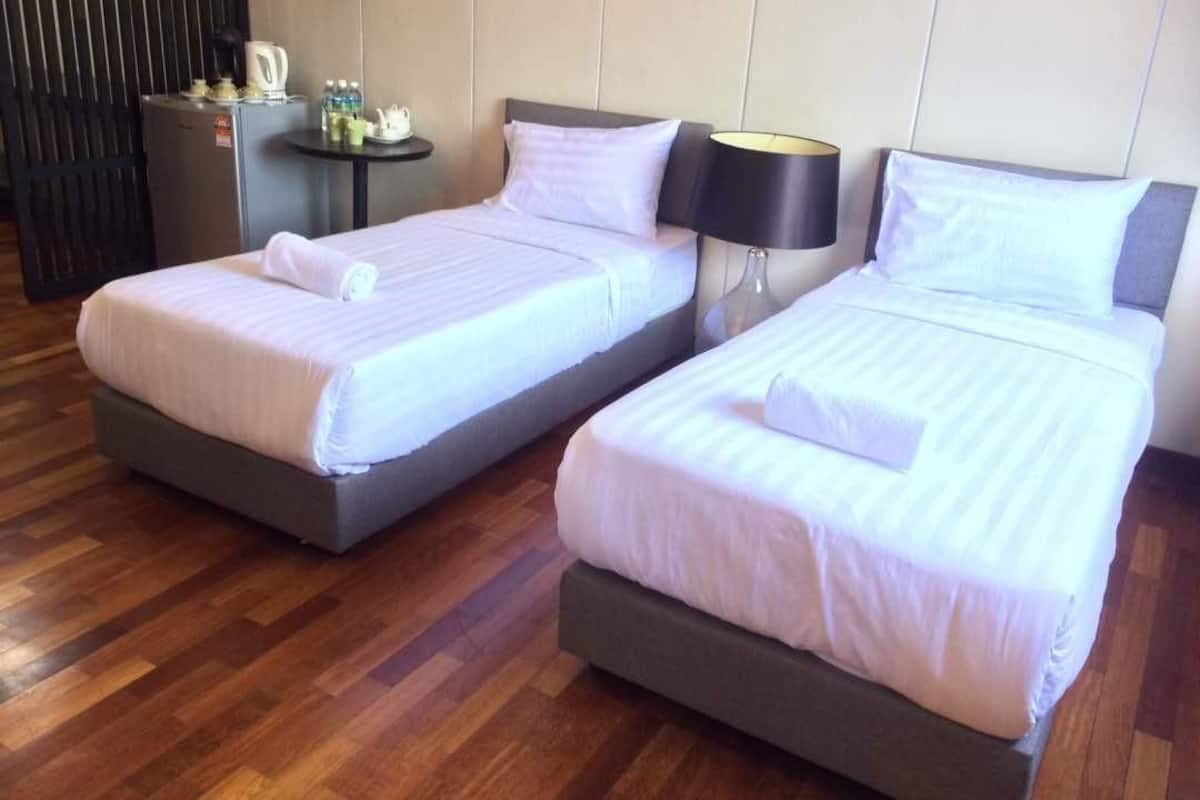 Two twin beds with white linens, a small table with a lamp, and a refrigerator.