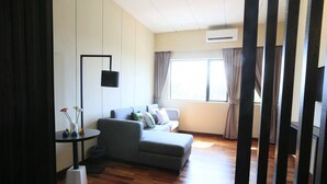 Uma sala de estar moderna com um sofá cinzento, uma mesa redonda pequena com objetos decorativos e uma janela grande com cortinas.