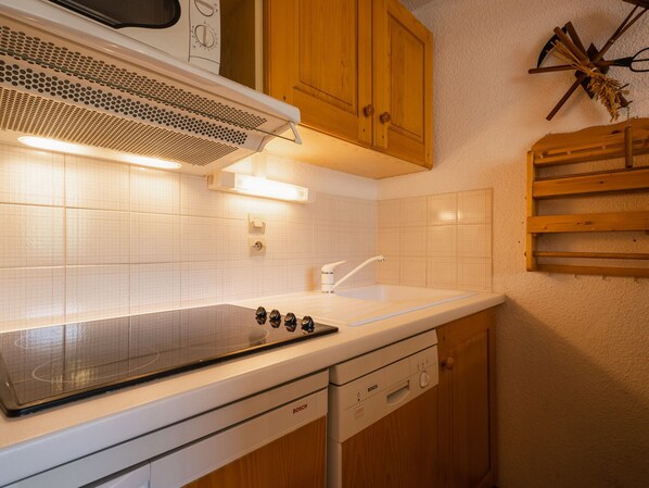 A kitchen with white tiles, a Bosch dishwasher, wooden cabinets, and a built-in stove. - 3* Apartment, 4-6 people, near slopes, pets allowed, garage (La Clusaz)