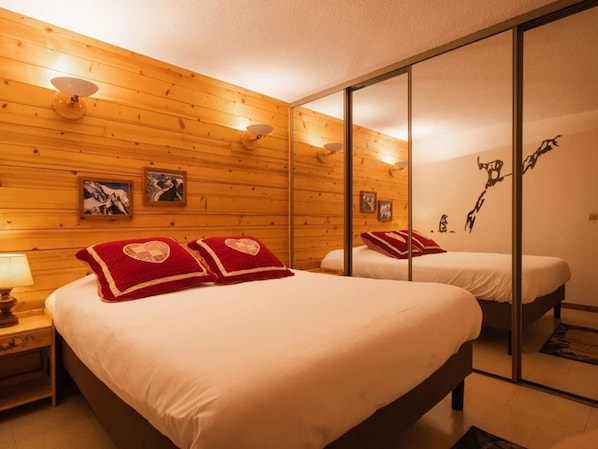 Habitación de hotel con paredes de paneles de madera, una cama grande con almohadas estampadas con corazones rojos, una mesita de noche con una lámpara y un espejo que refleja la habitación.