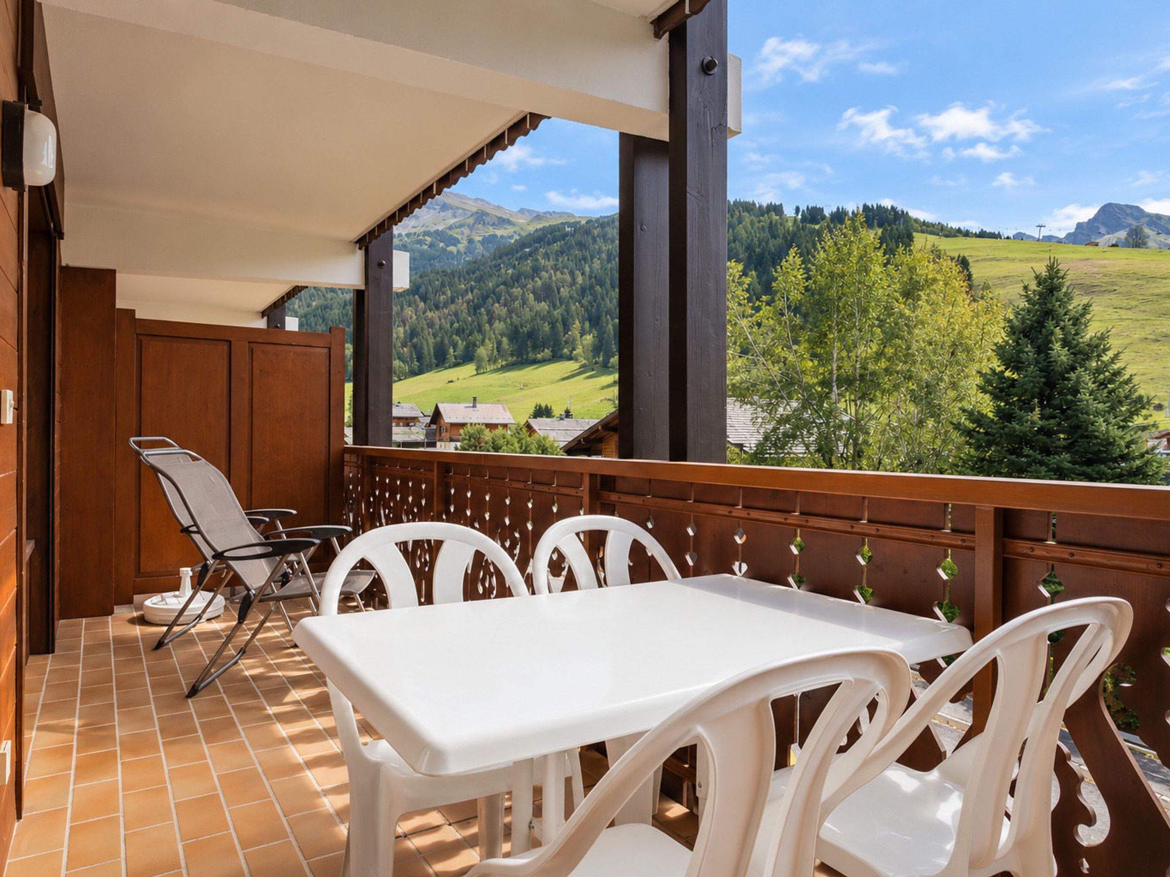 Ein Balkon mit einem weißen Tisch und Stühlen mit Blick auf eine gebirgige Landschaft.