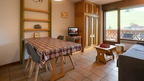 A dining area with a table set for two, a television, and a view of the outside.