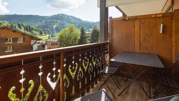 A balcony with a view of a mountain, a wooden fence, and a table with chairs.