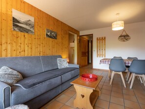 Ein Zimmer mit Holzwänden, einer Couch, einem Esstisch mit Stühlen und einem kleinen Holztisch mit einer roten Schüssel.