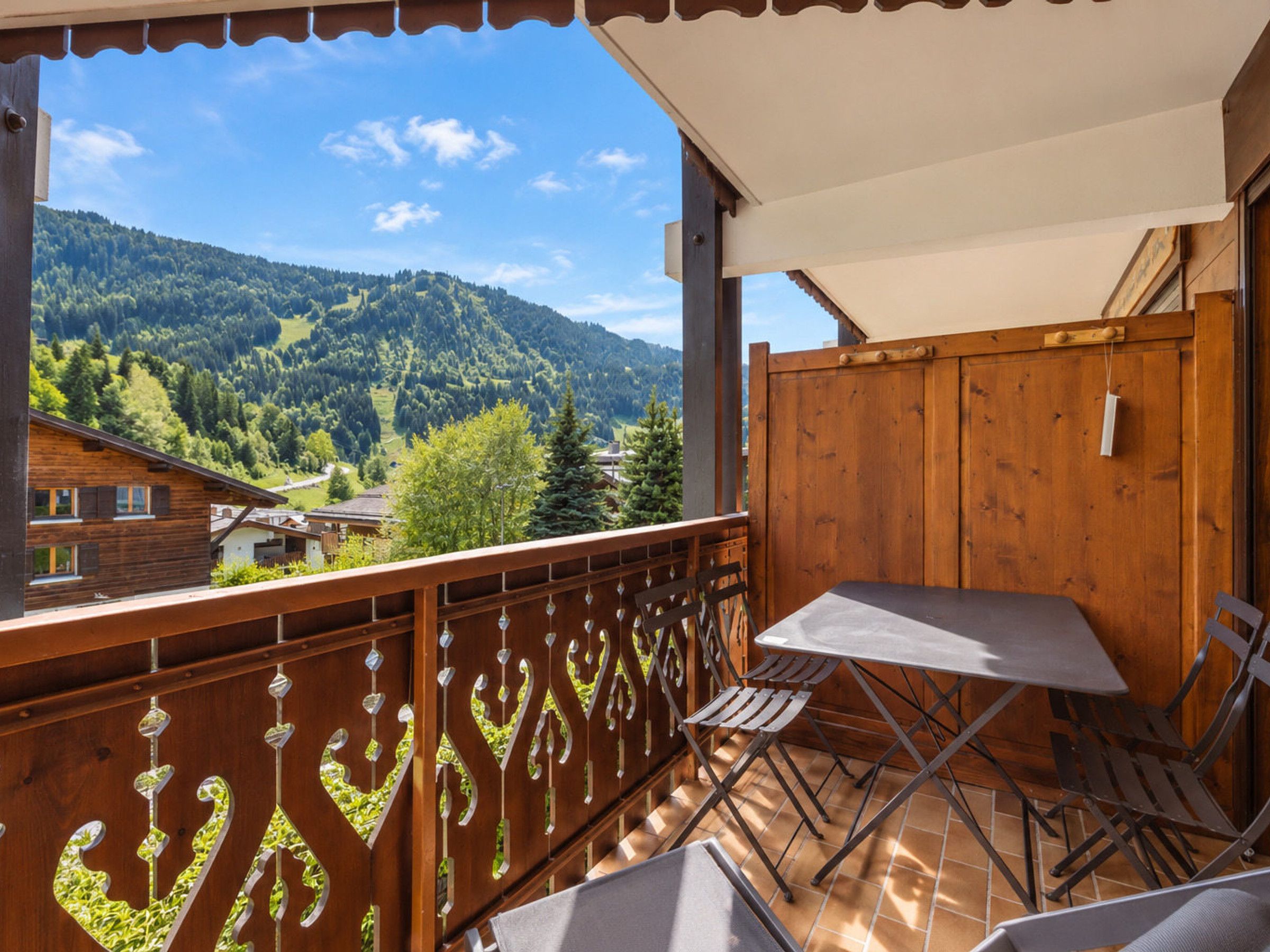 A balcony with a table and chairs, overlooking a mountainous landscape.