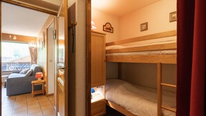 A room with a bunk bed, a sofa, a small table with a lamp, and a window with a view.