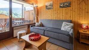 A cozy room with a grey sofa, a small wooden table, a red heart-patterned tray, and wooden walls.