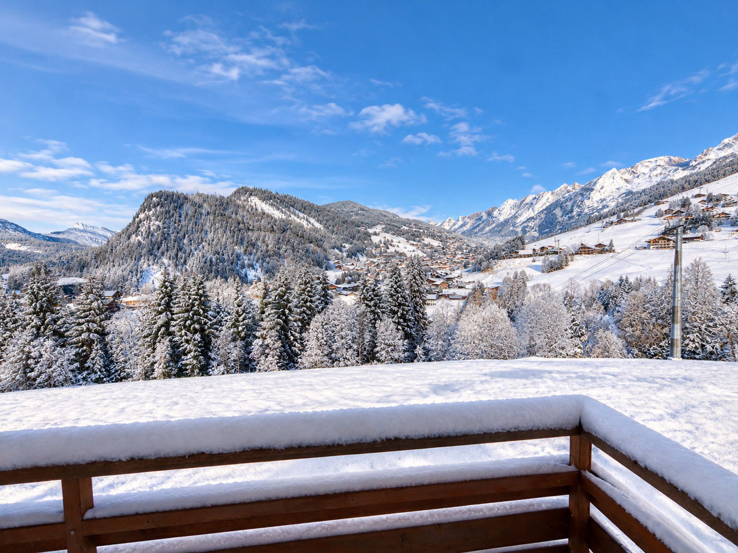 A wooden bench in a snowy landscape with a view of a mountain and a village.
