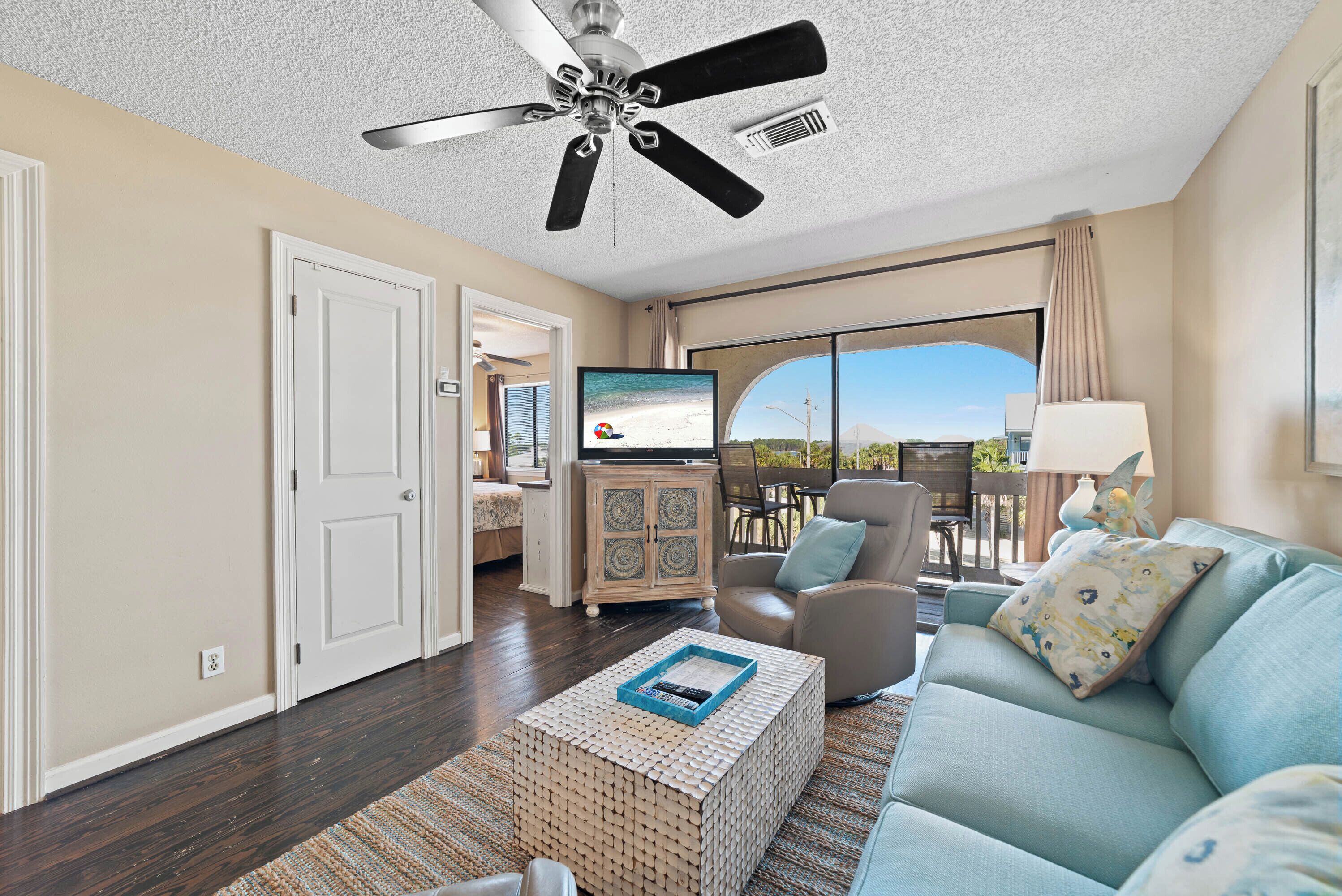 A spacious living room with a ceiling fan, a large TV, and a view to the outside. - Come Stay At This Cozy Beach Condo! (Gulf Shores)