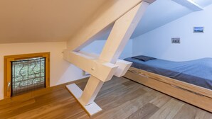 Une pièce avec un plafond en pente, un lit, une fenêtre avec des stores et un petit tableau accroché au mur.