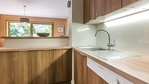 Une cuisine moderne avec des meubles en bois, un lave-vaisselle encastré et une fenêtre au-dessus du plan de travail, où se trouve un saladier.