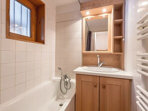 Uma casa de banho moderna com banheira, pia, armários de madeira, espelho e janela.