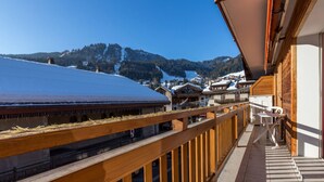 A balcony with a wooden railing overlooking a snowy mountain landscape.