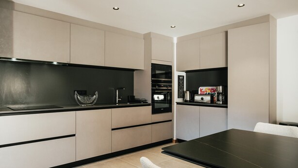 A modern kitchen with a black countertop, stainless steel appliances, and a dining area with a black table and white chairs.
