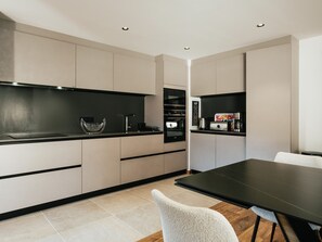 Eine moderne Küche mit schwarzem Arbeitsplatz, Edelstahlgeräten und einem Essbereich mit einem schwarzen Tisch und weißen Stühlen.