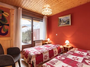Een kamer met twee bedden, een stoel, een houten plafond, een raam met uitzicht en een schilderij aan de muur.