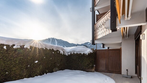 Un cortile innevato con una recinzione di legno, un balcone con ringhiera e una montagna sullo sfondo.