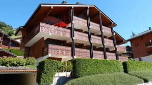 Un edificio a più piani con balconi, un garage e verde circostante.