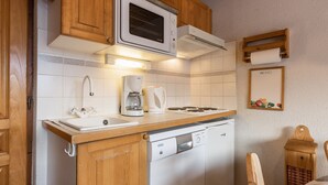 Una cucina compatta con mobili in legno, un forno a microonde, una macchina per il caffè, una lavastoviglie e un piccolo tavolo con una sedia.