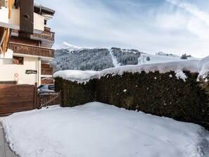 A snow-covered courtyard with a wooden fence, a hedge, and a building with balconies.