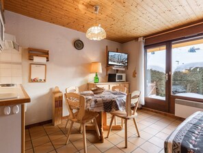 Um quarto acolhedor com teto de madeira, uma mesa de jantar com cadeiras, uma televisão e vista para uma paisagem nevada.