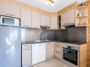 Una cocina moderna con gabinetes de madera clara, un refrigerador de acero inoxidable, un lavavajillas, un lavamanos y un horno.