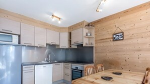Kompakti keittiö, jossa on modernit kodinkoneet, ruokapöytä ja puupanelointi.