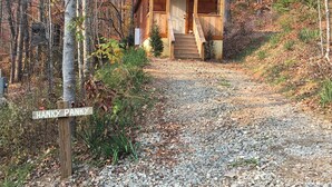Une cabane en bois dotée d’un porche et d’un chemin de gravier menant à l’entrée, le tout entouré d’un feuillage automnal.