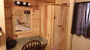 Une chambre dans un chalet en bois, comprenant un lit, un bureau, une chaise, une armoire et une fenêtre avec des rideaux.