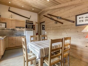 A rustic kitchen with wooden cabinets, a refrigerator, and a dining area with a table and chairs.