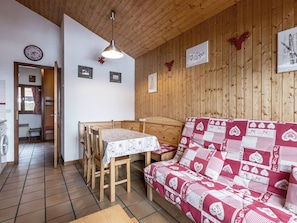 Una habitación acogedora con techo de madera, una mesa de comedor con sillas, un sofá estampado y un reloj de pared.
