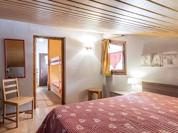 A bedroom with a bed, a chair, a small table, a mirror, and a door leading to another room. - Cozy 2-room with fireplace, near slopes, garage included (La Clusaz)