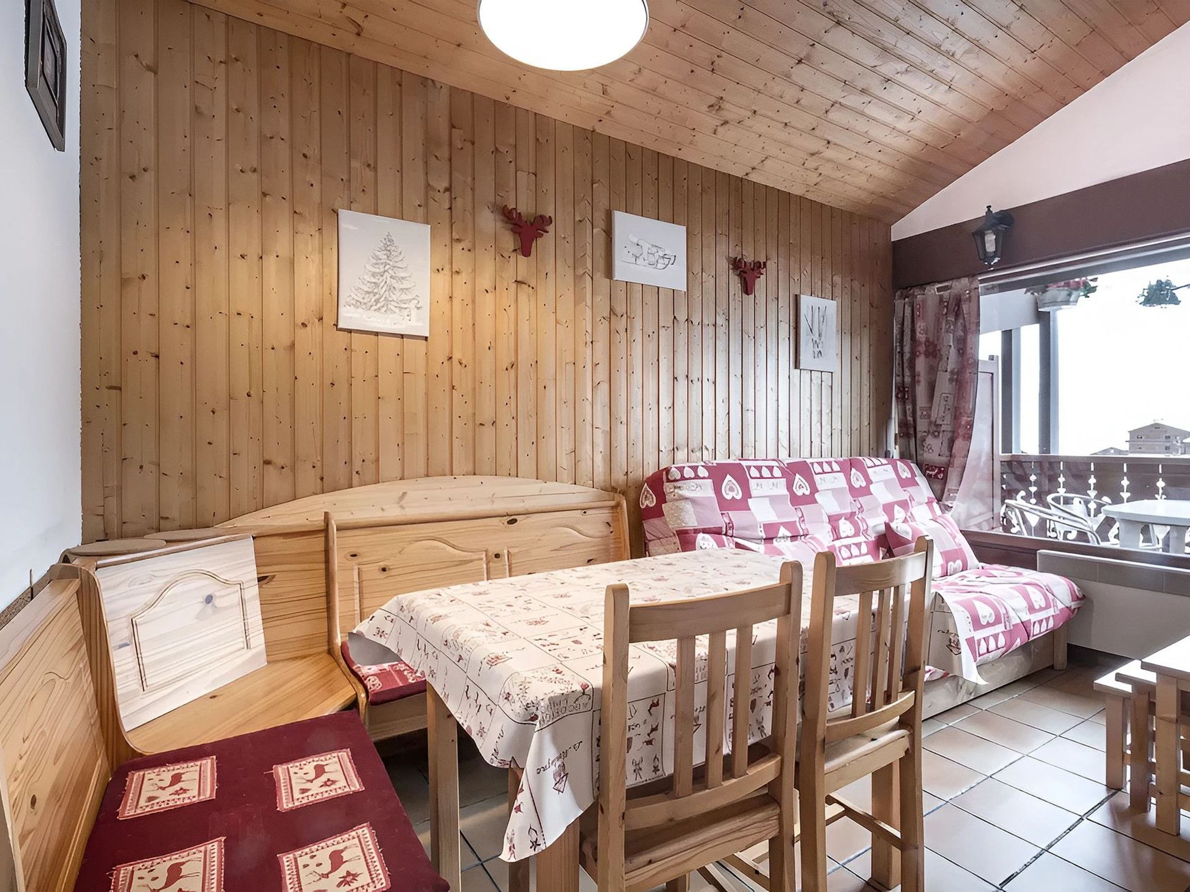 A cozy room with wooden walls, a bed with patterned bedding, a dining table with chairs, and a window with a view.