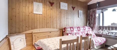 A cozy room with wooden walls, a bed with patterned bedding, a dining table with chairs, and a window with a view.