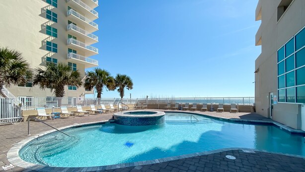 A swimming pool with a hot tub, lounge chairs, and palm trees. - NEWLY UPDATED FURNITURE! | Outdoor Pool | Hot Tub | Sauna | BEACHBALL PROPERTIES (Gulf Shores)