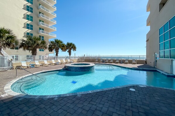 A swimming pool with a hot tub, lounge chairs, and palm trees. - NEWLY UPDATED FURNITURE! | Outdoor Pool | Hot Tub | Sauna | BEACHBALL PROPERTIES (Gulf Shores)