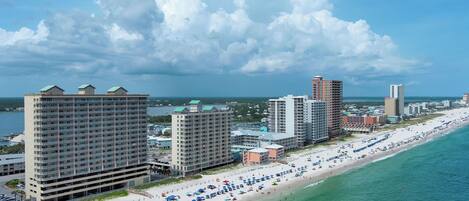 A coastal cityscape with a beachfront hotel, high-rise buildings, and a crowded beach.