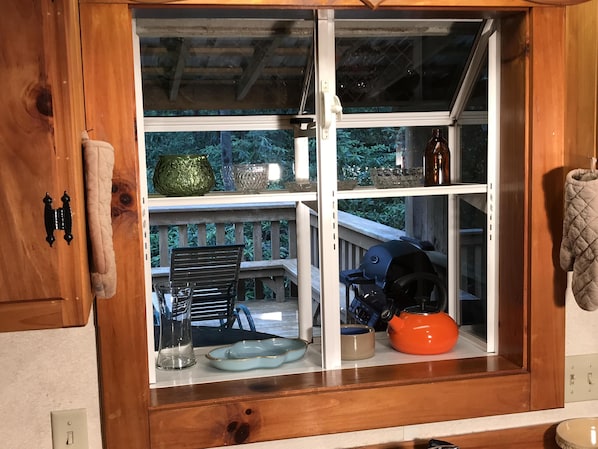 A kitchen with a window view of a deck, a grill, and various kitchen items.
