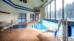 En inomhuspool med utsikt över träd utanför, ett tegelgolv och ett bord med stolar.